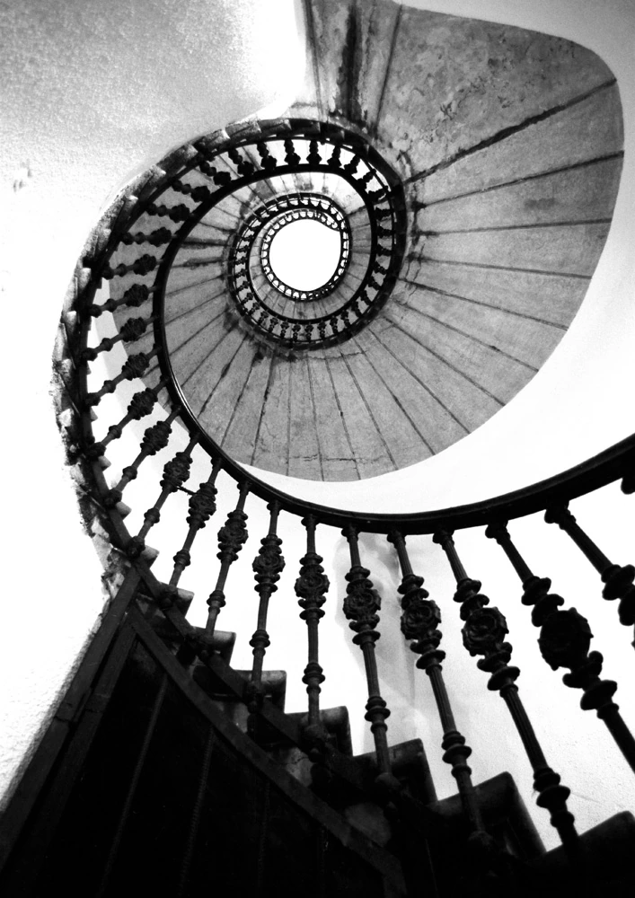 Black and white fine art photograph looking up through a spiral staircase in Budapest, emphasising repeating circular geometry.